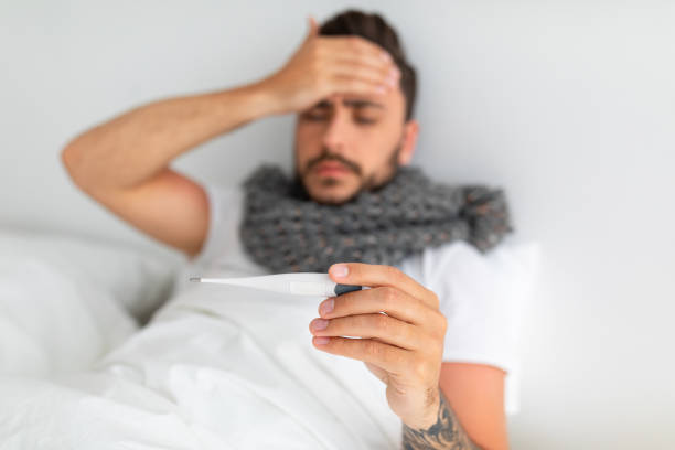istock Sick man checking body temperature holding thermometer and touching forehead, sitting on bed at home, selective focus 1342243132