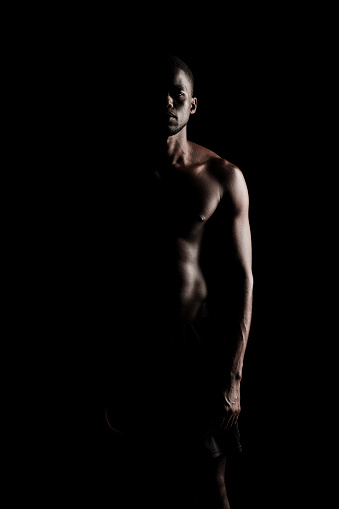 Bare chested black fitness man silhouette looking at camera wearing sport short trousers on black backgorund