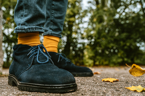 Close-up of legs in blue suede shoes and yellow socks. Asphalt with fallen leaves. Autumn fashion for men.