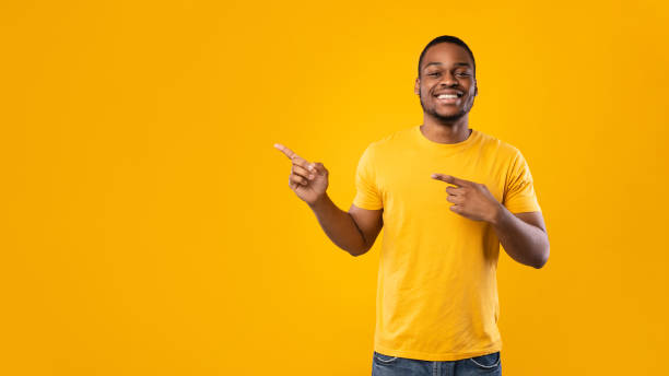 istock Cheerful African Man Pointing Fingers Aside Over Yellow Background, Panorama 1342245334