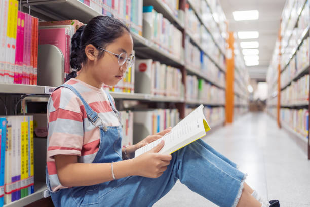 図書館で本棚の本を読む小さな女の子 - bookstore student chinese ethnicity book ストックフォトと画像