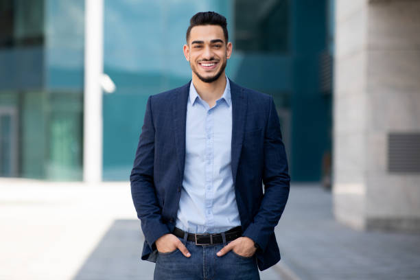 Handsome middle-eastern guy businessman posing next to office center Handsome middle-eastern guy young businessman in stylish suit posing next to office center, smiling arab entrepreneur having break after successful busienss meeting, standing on street, copy space businessman stock pictures, royalty-free photos & images