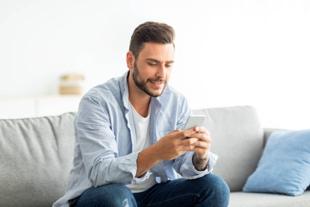istock Useful app concept. Millennial man using modern smartphone while sitting on sofa in living room, free space 1342247181