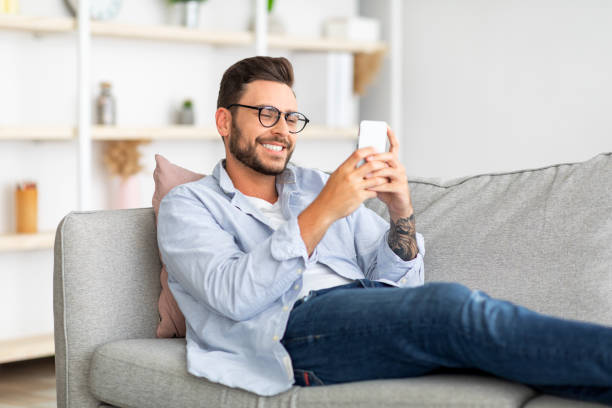 istock Great mobile app. Happy guy using smartphone, texting and surfing social networks, sitting on couch, copy space 1342247977