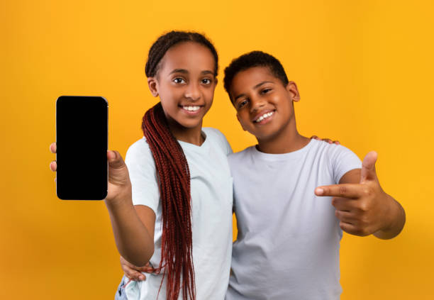 entzückende schwarze teenager bruder und schwester zeigen smartphone, mockup - twin tips stock-fotos und bilder