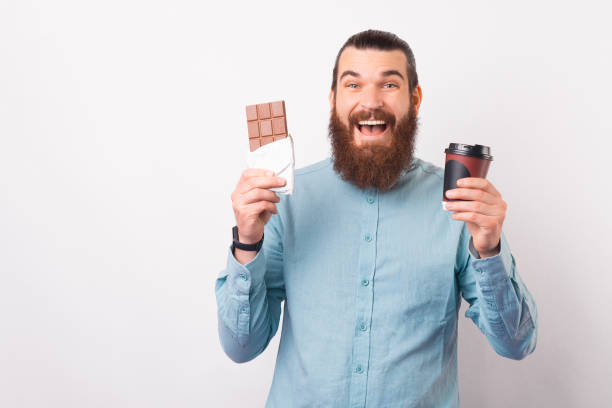istock Joyful bearded man is holding a chocolate bar and a paper cup. 1342248291