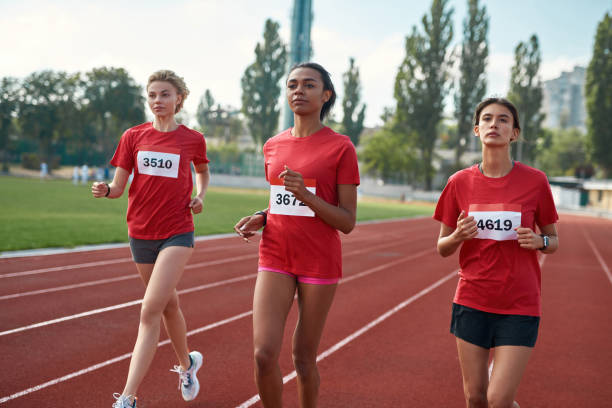 jeunes femmes athlétiques courant ensemble pendant le championnat d’athlétisme au stade un jour d’été - track and field athlete women vitality speed photos et images de collection