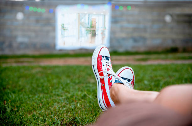American flag sneakers shoes on ground and textile movie screen in open cinema in the green backyard. Female Enjoying and relaxing on Summer weekend, watching TV in open air. Copy space