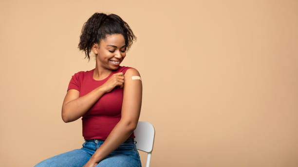 istock Cheerful vaccinated Afro woman showing plaster on her shoulder after immunization against covid over beige background 1342251990