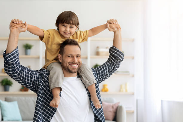 istock Cheerful father riding his little son on shoulders, having fun together at home, both smiling to camera, empty space 1342252021