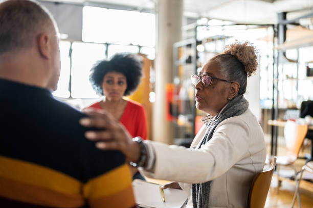 donna anziana che conforta un uomo maturo in terapia di gruppo in un coworking - mano sulla spalla foto e immagini stock