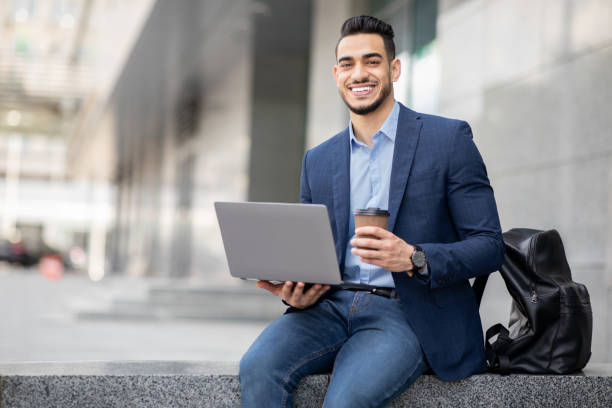 istock Positive middle-eastern guy with laptop having coffee break outdoors 1342252441