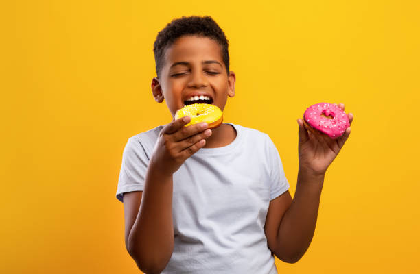 istock Black boy holding colorful donuts, isolated on yellow background 1342252592