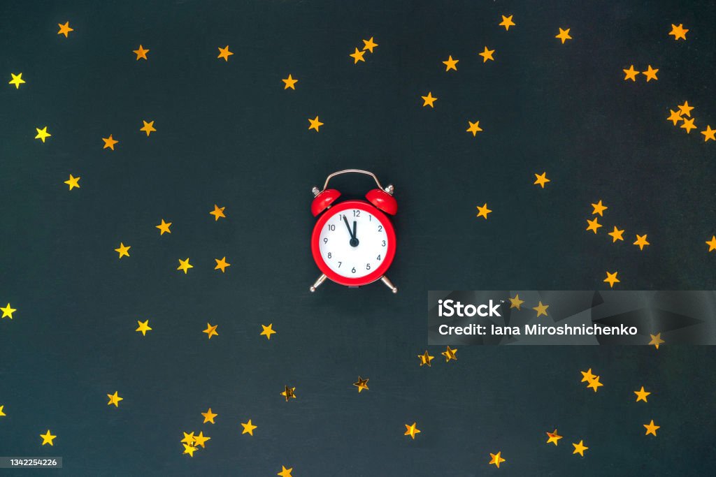 Christmas composition with red alarm clock twelve and golden stars confetti on black background. New Year, Christmas holiday. 12 O'Clock Stock Photo