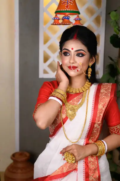 Portrait of beautiful Indian Bengali female woman in red and white traditional ethnic saree and jewellery in studio lighting indoor. Indian culture, religion and fashion
