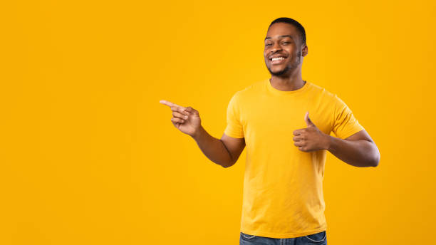 istock African American Guy Pointing Finger Aside Gesturing Thumbs-Up, Yellow Background 1342254676