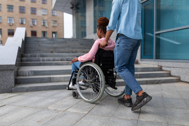 istock Black guy pushing wheelchair with handicapped woman, having problem entering building, standing near stairs without ramp 1342255515