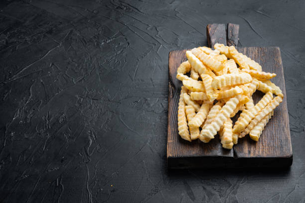 istock Frozen oven chips sliced potato, on wooden cutting board, on black background , with copyspace  and space for text 1342255842