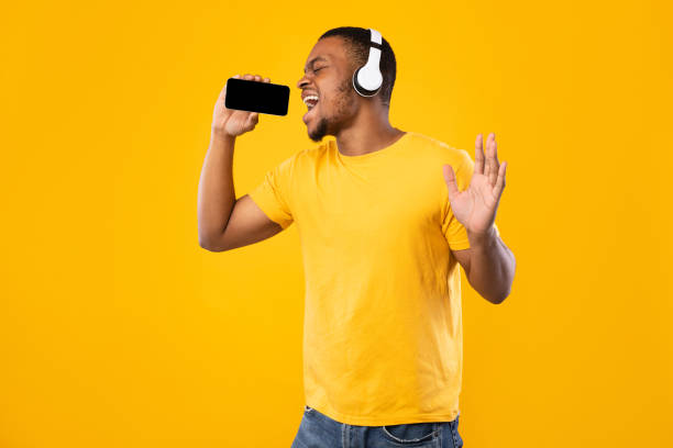 istock Black Man Singing Holding Smartphone Like Microphone On Yellow Background 1342256173