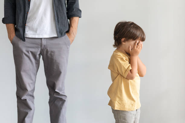 Little baby boy crying alone, feeling lonely and abandoned, unrecognizable indifferent father standing behind stock photo