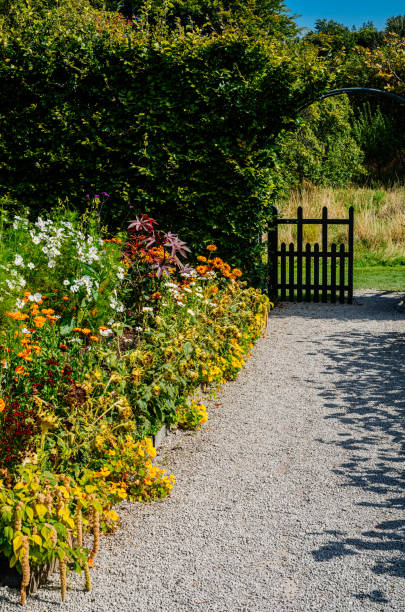 Garden path leading past a colourful flowerbed to a wooden gate in the English countryside.