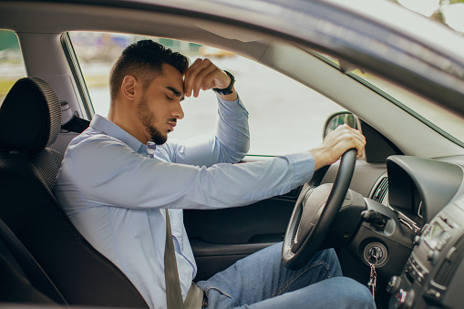 Car accident concept. Upset arab businessman driver sitting at front seat and touching his head, having automobile crash. Middle-eastern guy getting late for flight, got stuck in traffic, side view