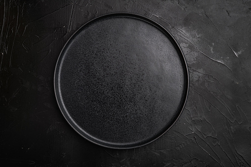 Top view of black plate set, on black dark stone table background