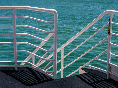 White handrails along stairs, with shadows on carpeted deck, on a forward side of a small interisland cruise ship on a sunny day along the Gulf Coast of Florida