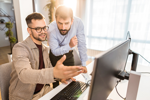 Two work colleagues having a discussion and brainstorming together while working on a computer in office.