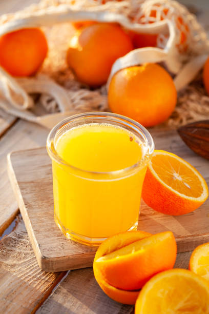 glass of freshly sqeezed orange juice on a wooden table. natural source of vitamins, healthy beverage for ideal breakfast. bright sunny summer day. close up, copy space for text. - freshly squeezed orange juice imagens e fotografias de stock