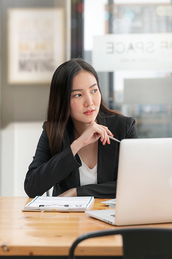 Portrait of young businesswoman with hand touch her chin and sitting at office desk, vertical view.