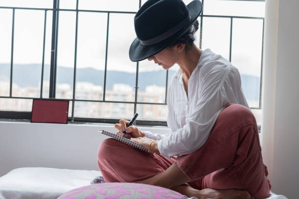 Beautiful woman sitting by the window writing to a poet enjoying her hobby Beautiful Latin from Bogotá Colombia between 30 and 34 years old, sitting next to the window writing a poet enjoying her hobby poet stock pictures, royalty-free photos & images