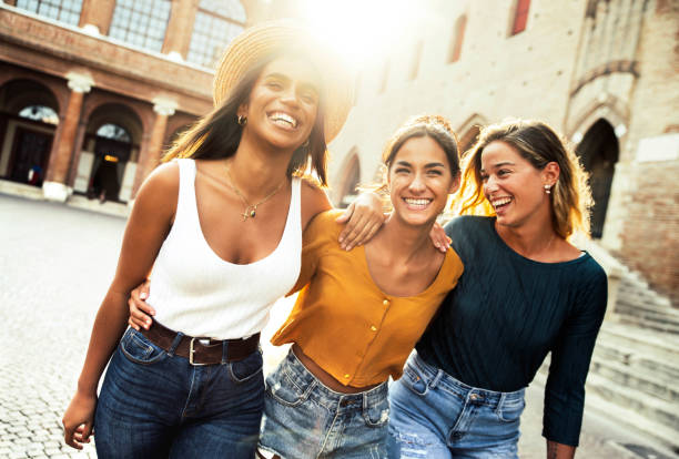 Three young diverse women having fun on city street outdoors - Multicultural female friends enjoying a holiday day out together - Happy lifestyle, youth and young females concept stock photo
