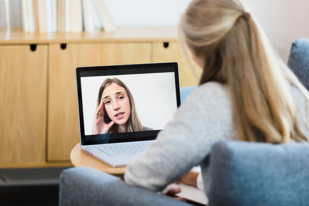 Exhausted young woman shares with female counselor via tele-therapy The exhausted young adult woman shares with the unrecognizable female therapist via video call. melancholy computer support specialist stock pictures, royalty-free photos & images