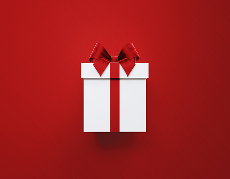 White gift box tied with red ribbon on red background. Horizontal composition with copy space. Great use for Christmas and Valentine's Day related gift concepts.