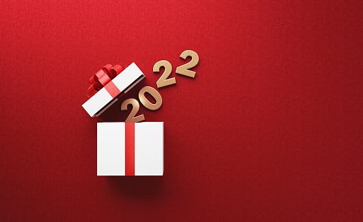 Gold colored 2022 is coming out of a white gift box tied with red ribbon on red background. Horizontal composition with copy space. Directly above. Great use for Christmas related gift concepts.