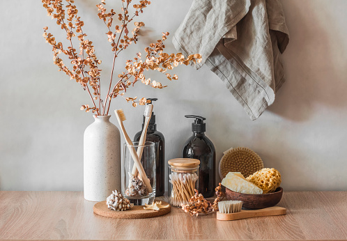 Bathroom interior still life. Decorative flowers, shampoo bottles, cotton buds, brushes, soap, towels on a wooden background. Minimalism interior