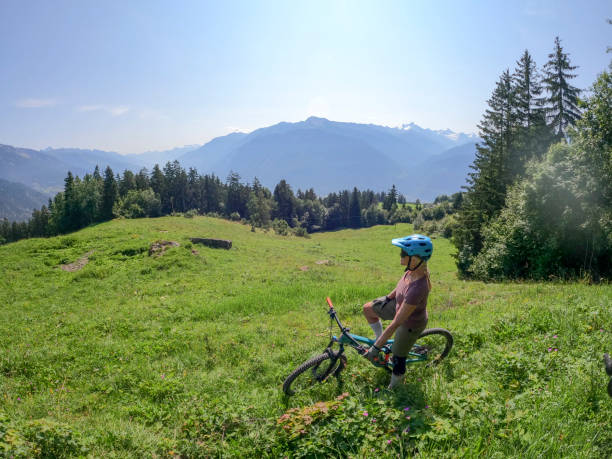 Female mountain biker relaxes in sunny meadow She looks off towards European Alps in the distance crans montana stock pictures, royalty-free photos & images