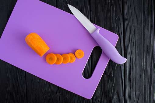 Sliced carrots  on the purple cutting board  on the black wooden background. Top view. Close-up. Copy space. Diet minimal concept.