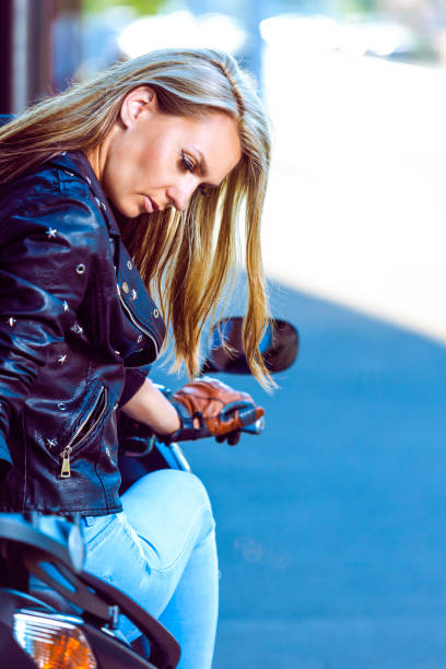 istock Sensual Sexy Caucasian Female Biker in Leather Outfit While Posing With Tilted Head in Front of Shiny New Bike Outdoors. Vertical Image Composition 1342302046