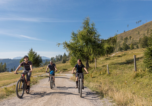 A small group of three mountainbikers is riding uphill side by side on a gravel road on a scenic pasture area nearby Lake Weißensee which is a lake in the Austrian state of Carinthia within the Gailtal Alps mountain range. It is the highest situated (930 mts., 3051 ft.) Carinthian bathing lake. In the wintertime the lake is very famous for ice-skating.\nCanon EOS 5D Mark IV, 1/250, f/16, 24 mm.