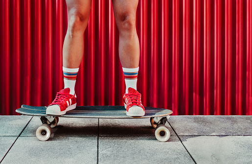 detail of a woman's legs on a skateboard. the girl has high socks and red sneakers. the background is red.