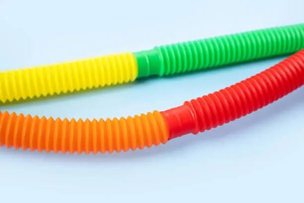 Photo of Colorful anti-stress fidget push pop tube sensory toys for children on blue background. Top view, flat lay. Close-up of creative game with popular plastic flexible bright corrugated pipe.