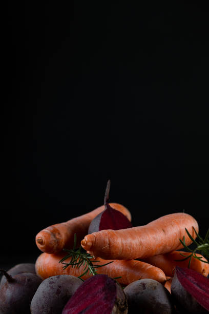 Carrots, beets and rosemary arranged on a wooden surface and black background.