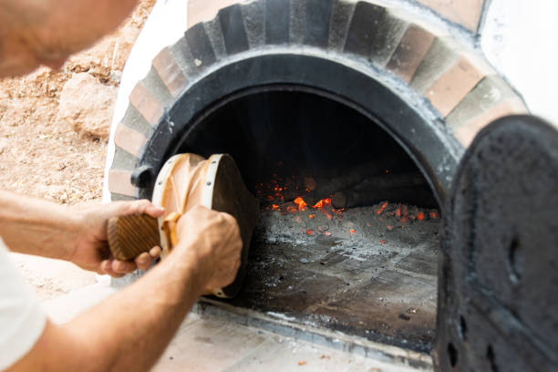 Artisan wood-fired oven and man's hands blowing the embers with a bellows White painted artisan wood-fired oven built on the outside with the door open and man's hands blowing the embers with a bellows bellows stock pictures, royalty-free photos & images