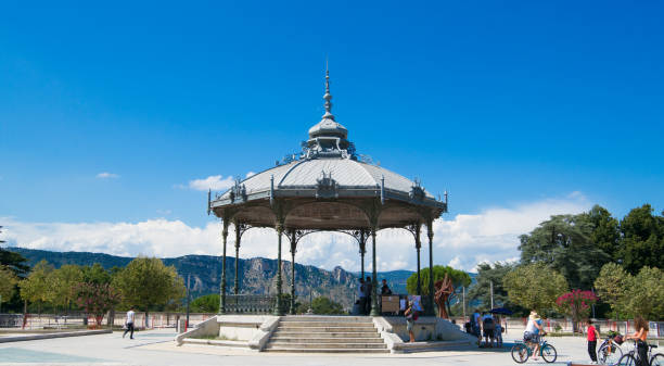 Peynet kiosk in Valence with hills at the background and blue sky Peynet kiosk in Valence with hills at the background, small group of people walking, cycling around rotunda photos stock pictures, royalty-free photos & images