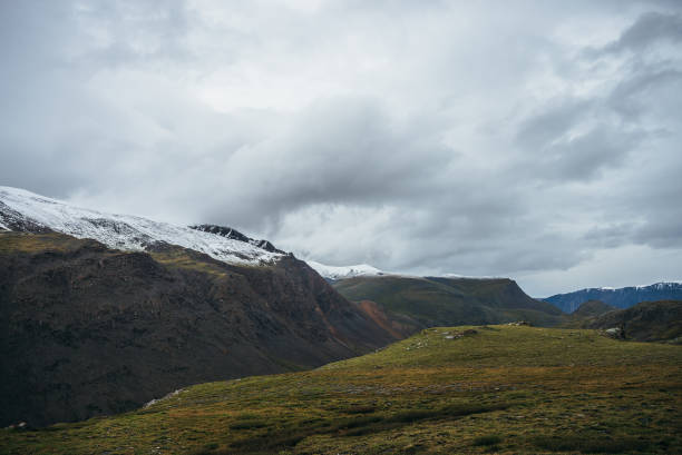 istock Atmospheric alpine landscape with deep gorge and snow-capped multicolor mountains in overcast weather. Beautiful scenery with snowbound mountain range under cloudy sky. Motley high mountains with snow 1342351139
