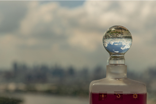 Looking through crystal ball on the top of glass bottle showing an upside down skyline. Refraction photography, copy space. Selective focus.