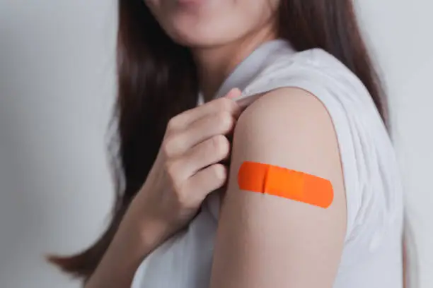 Teenager asian woman showing off an orange bandage after receiving the covid-19 vaccine. Vaccination campaign concept for safe life return to normal life.