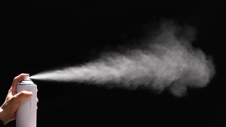 Slow motion speed closeup scene in side view of aerosol can when spraying, white color spray isolated on black background